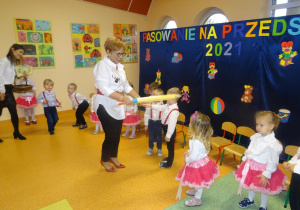 Pani dyrektor Maria Królikowska trzyma w ręku żółtą kredkę, którą przykłada chłopcu do lewego ramienia.